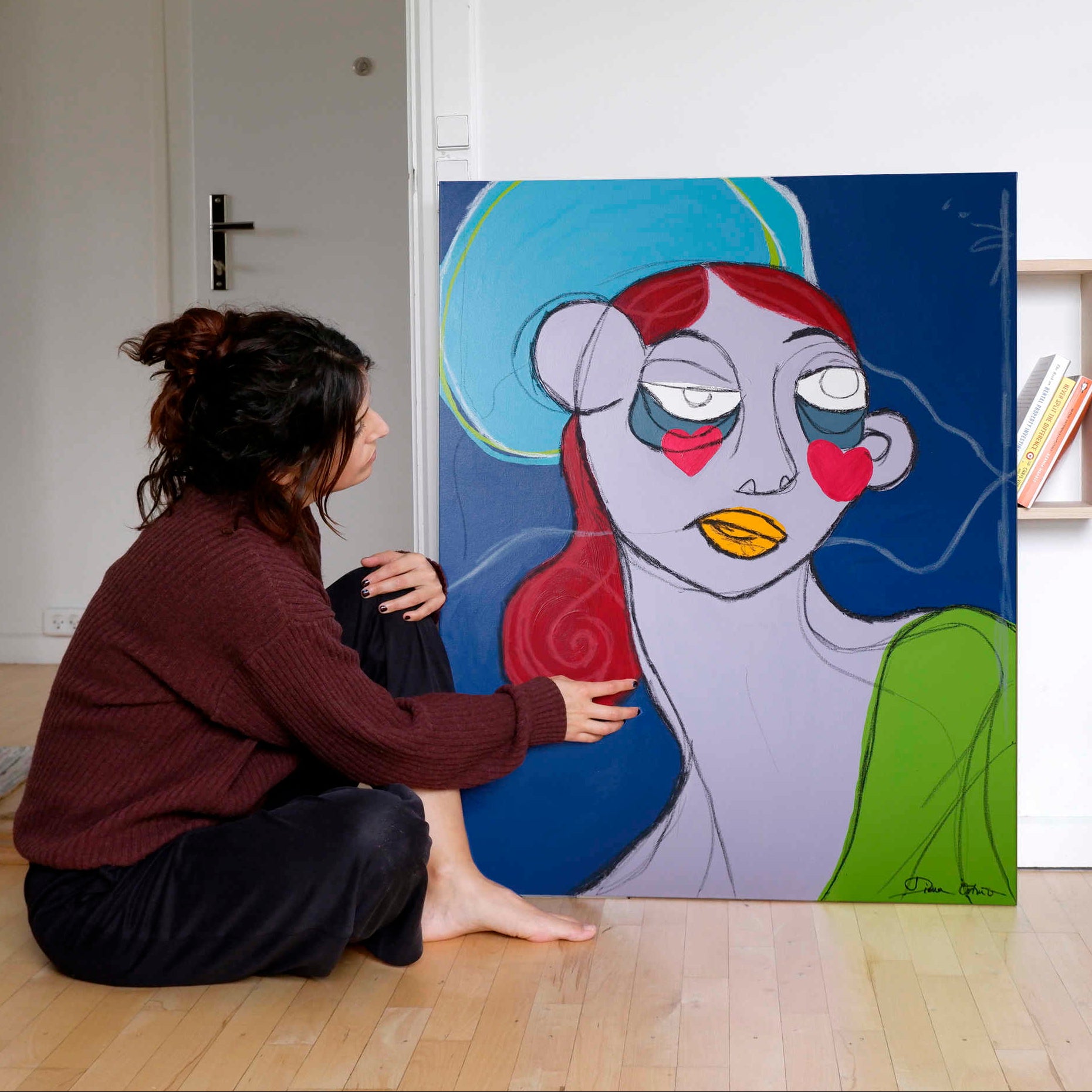 Artist interacting with a colorful painting of an expressive woman on a white wall